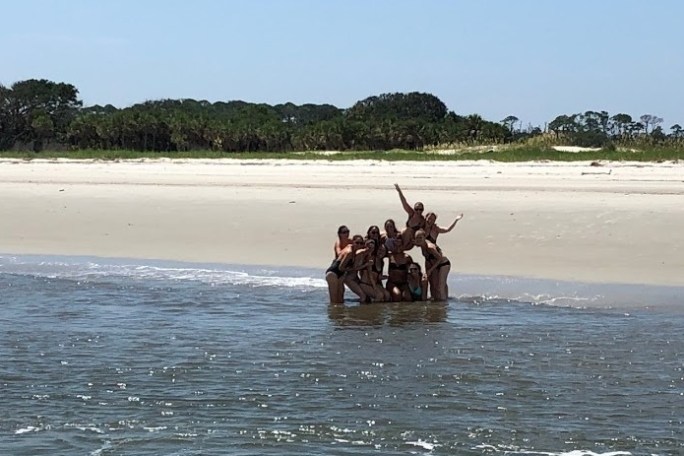 Group of people posing by the water on a sandy beach.