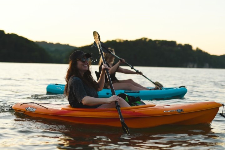 Two people kayaking on a calm lake at sunset.