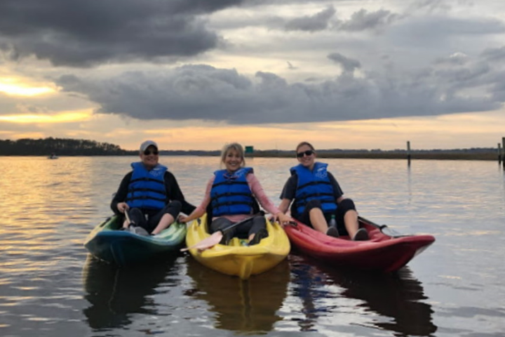 Three people in kayaks on a calm lake at sunset, wearing life jackets.