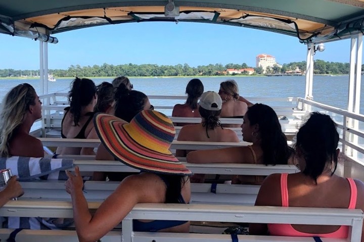 Group of people on a boat with a view of the water and distant shoreline.