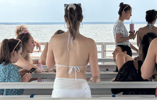 Women in swimsuits talking and sitting on a boat under a cloudy sky.